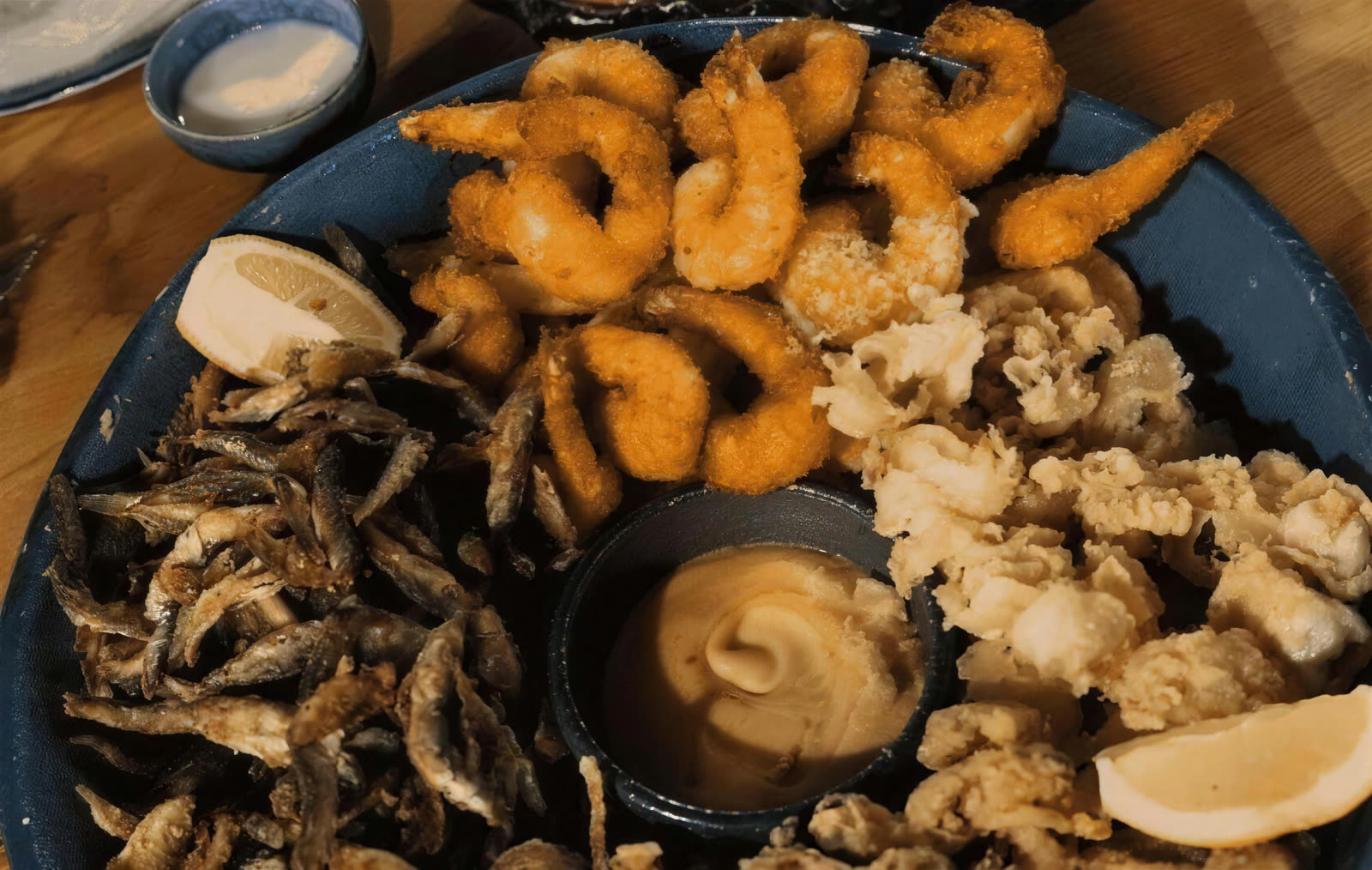 Platou prăjit servit la ei: creveți pane, calamari baby, peștișori și midii, cu sos în mijloc